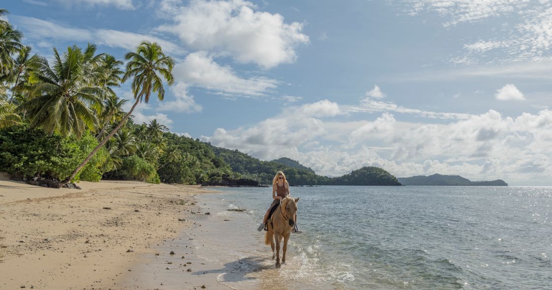 A Man Riding A Horse On A Beach